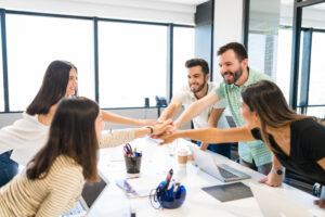 Happy business people celebrating success while stacking hands in motivational meeting at office